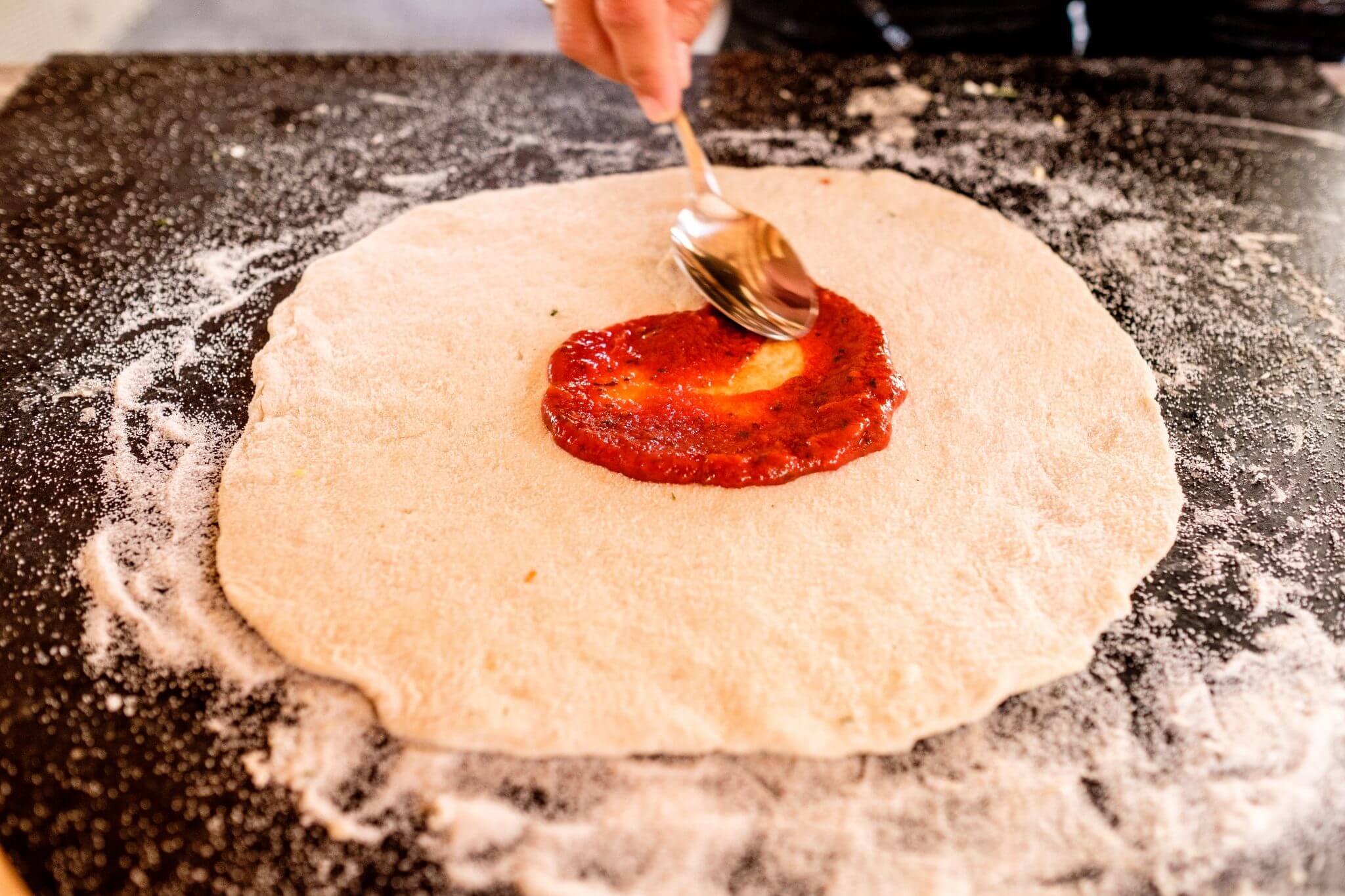 Zelfgemaakte pizzasaus op een verse pizzabodem smeren